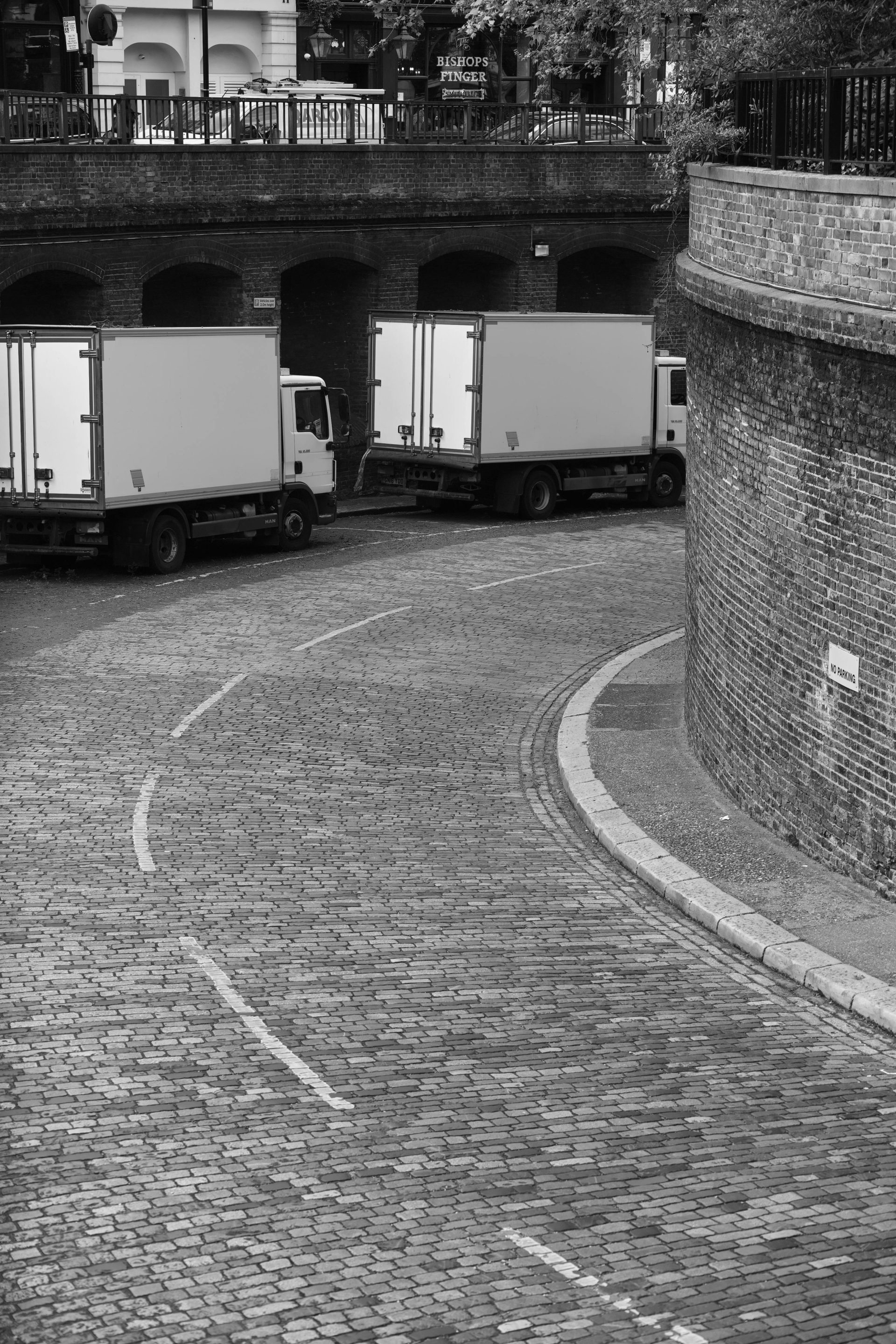 Monochrome urban scene showing paved city street with trucks and brick structures.